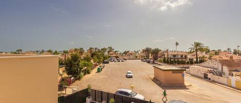 Zona residencial con cielo despejado, palmeras y una calle con coches estacionados.