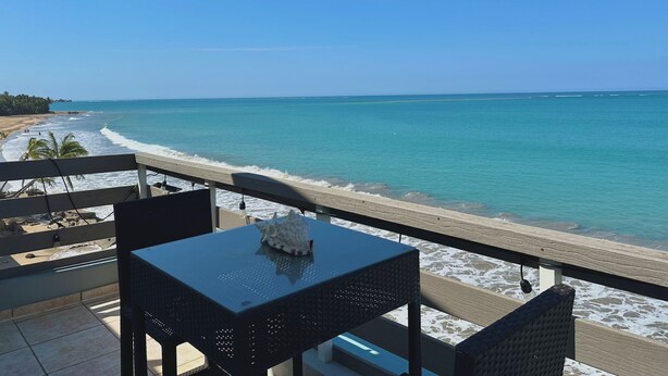 Un balcon avec une table et des chaises donnant sur une plage et l’océan.