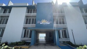 L’entrée d’un hôtel, avec une façade bleue et blanche, une enseigne indiquant « Belle Mar » et un ciel dégagé au-dessus.