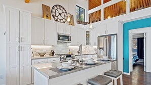 A modern kitchen with white cabinetry, a central island with stools, and a view to the dining area. - Lakefront, 1 King Bed, dock, mist view, electronic firepit (Lower Lake)