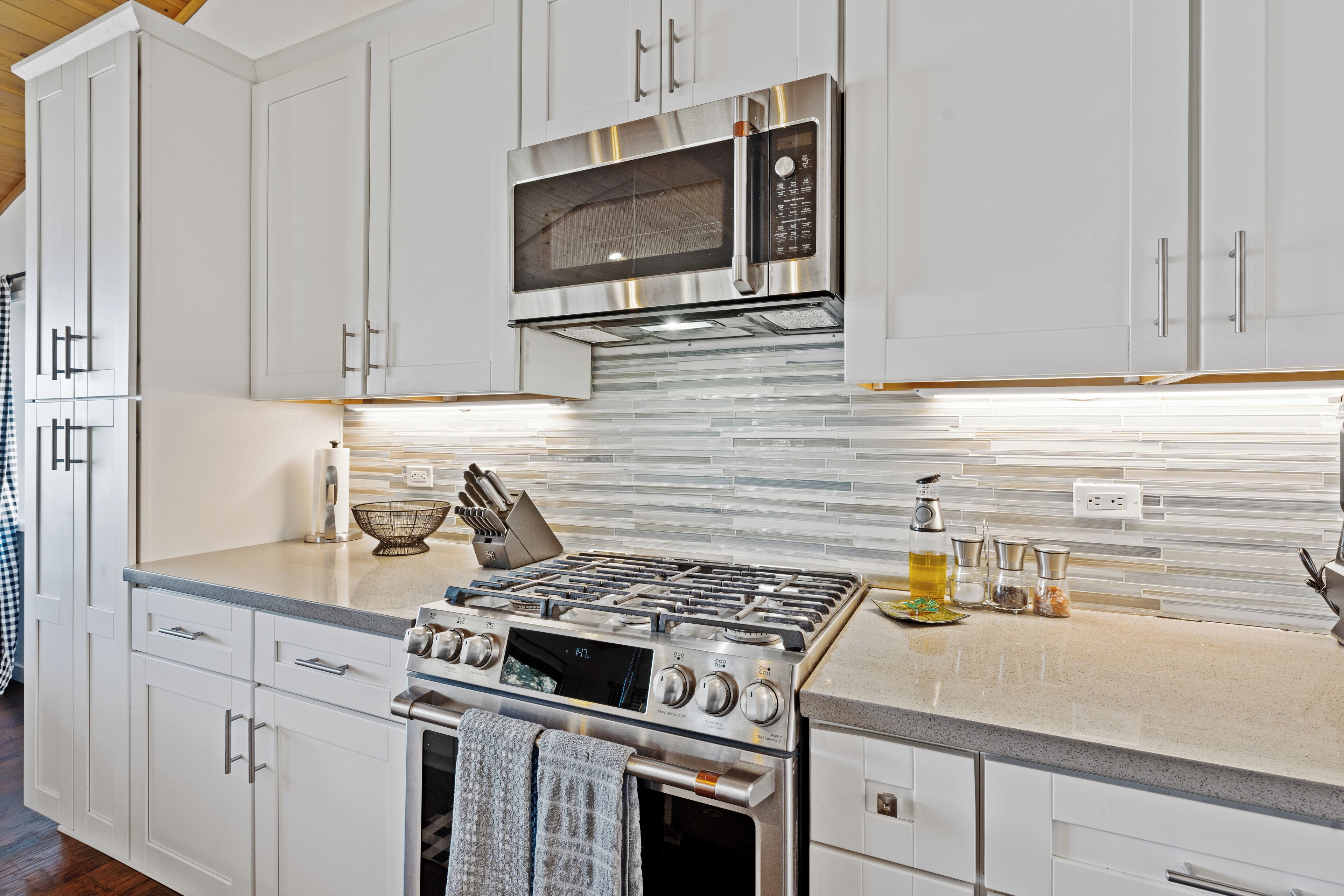 A modern kitchen with white cabinets, a stainless steel stove, and a microwave.