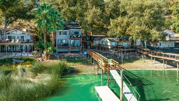 A waterfront property with multiple buildings, a dock, and a palm tree. - Lakefront, 1 King Bed, dock, mist view, electronic firepit (Lower Lake)