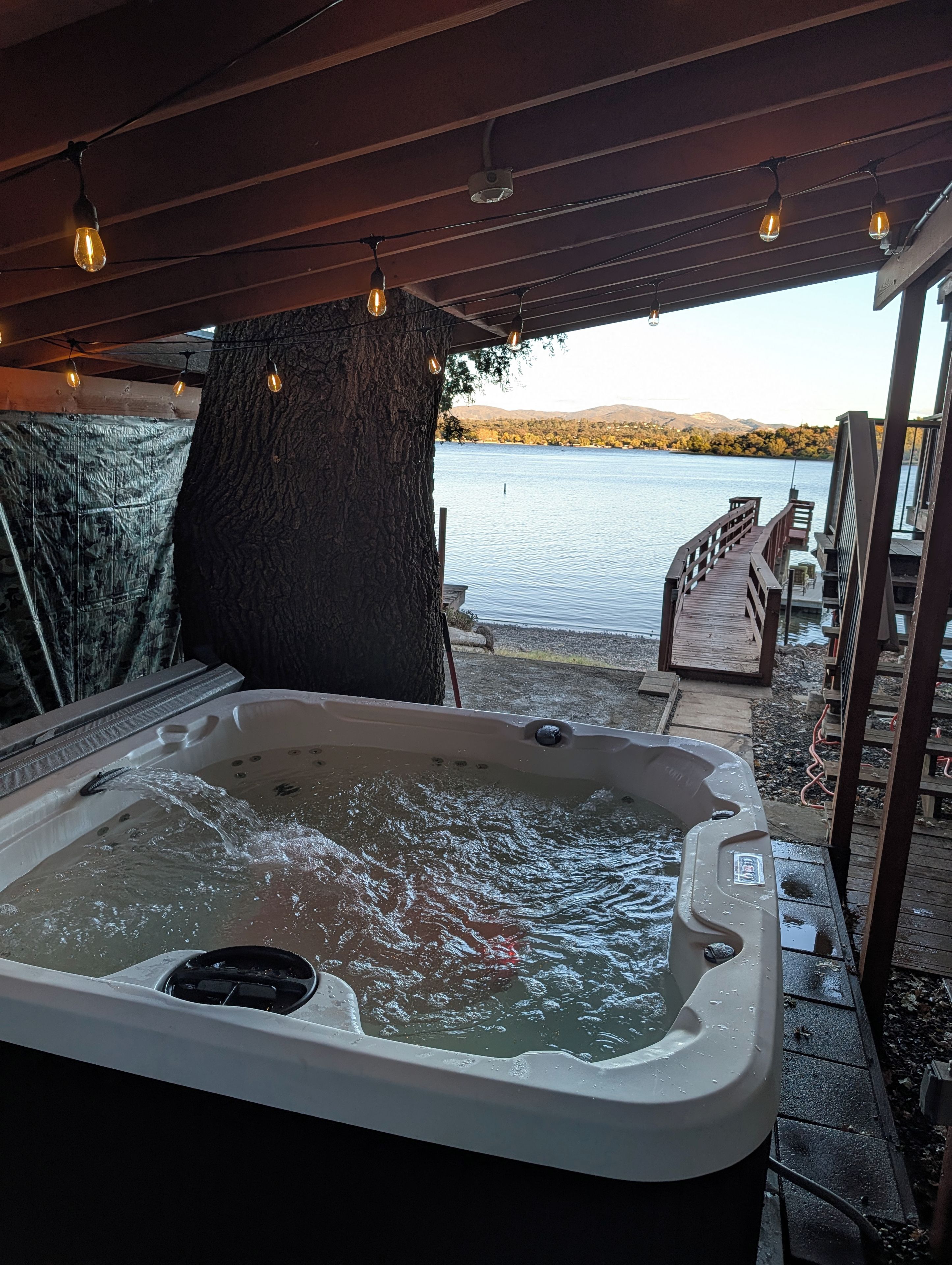 A hot tub with water flowing, a wooden deck, and a view of a lake and mountains.