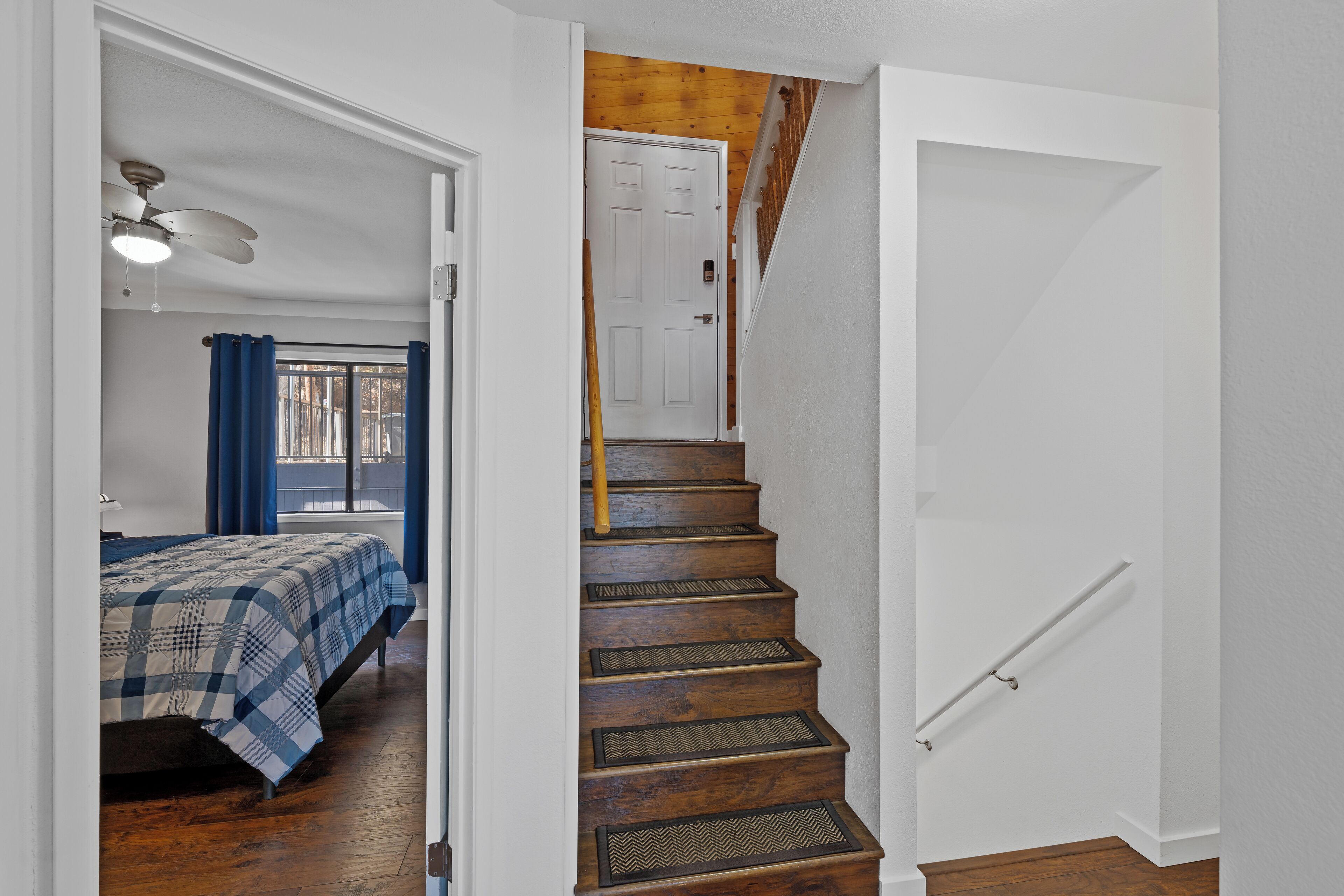 Una escalera de madera con barandilla que lleva a una habitación con cama y ventilador de techo.