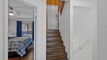 Una escalera de madera con barandilla que lleva a una habitación con cama y ventilador de techo.