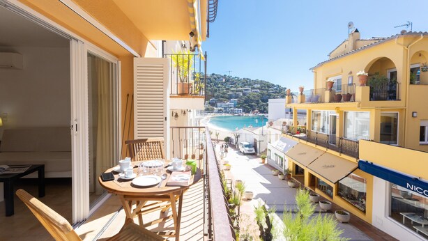 Ein Balkon mit Esstisch, der auf eine Küstenlandschaft mit Gebäuden und Strand blickt.