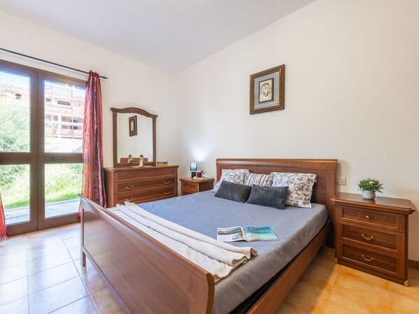 Une chambre à coucher avec un lit, une table de chevet, une commode, un miroir et une fenêtre avec des rideaux.