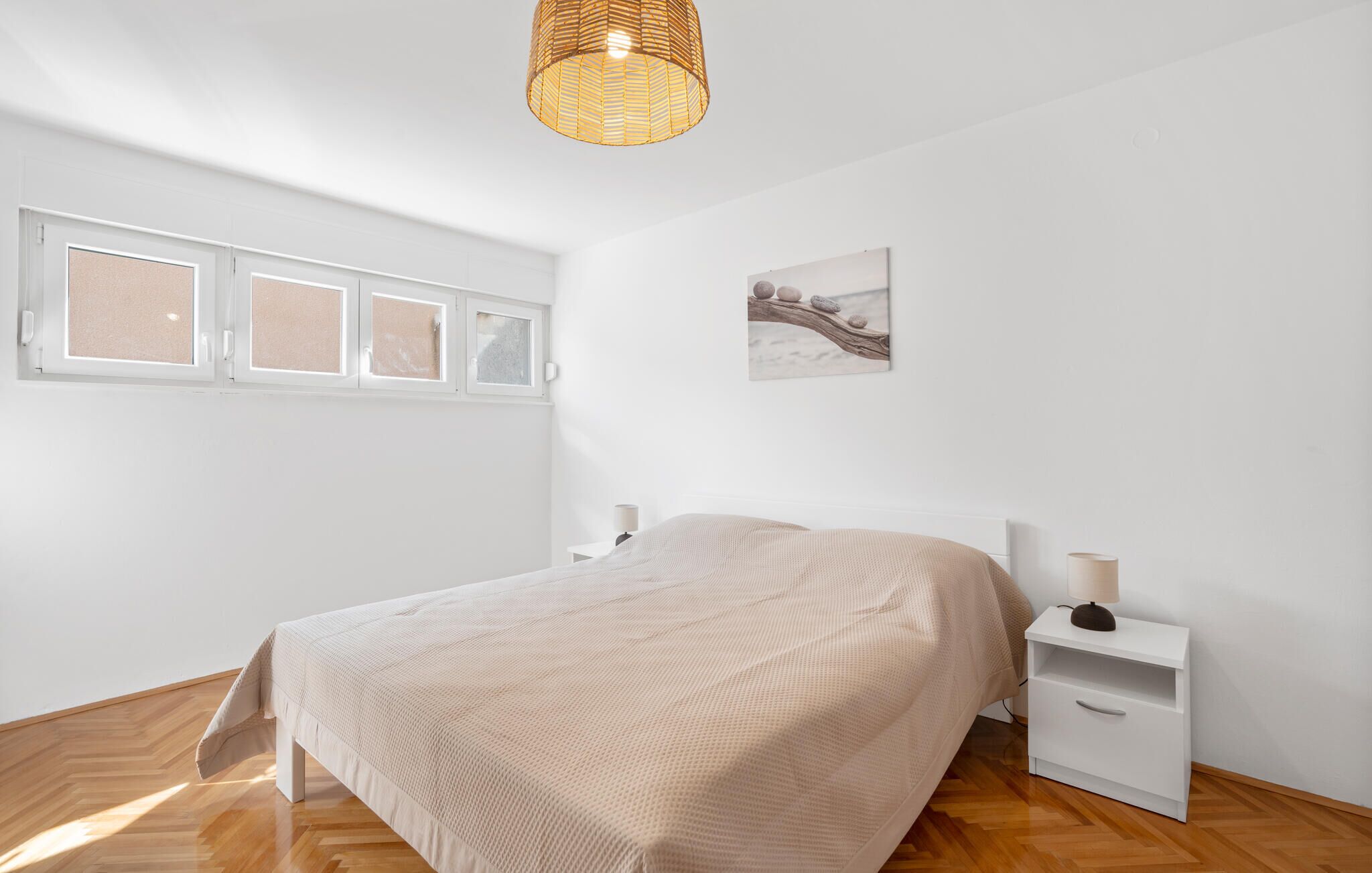 A bedroom with a bed, a nightstand, a lamp, a window, and a wall-mounted picture.