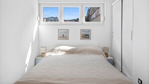 Un dormitorio con una cama, dos mesitas de noche, un ventanal con vistas a tres paisajes y dos cuadros en la pared.
