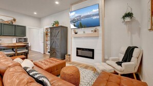 A living room with a fireplace, a television mounted above it, and a comfortable seating area with sofas and a chair. - Spacious Cottage -Hot Tub, Patio, Fire Table, WIFI (Central Point)