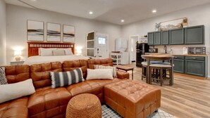A modern living room with a brown leather sofa, a wooden coffee table, and a kitchen area with green cabinets and a microwave. - Spacious Cottage -Hot Tub, Patio, Fire Table, WIFI (Central Point)