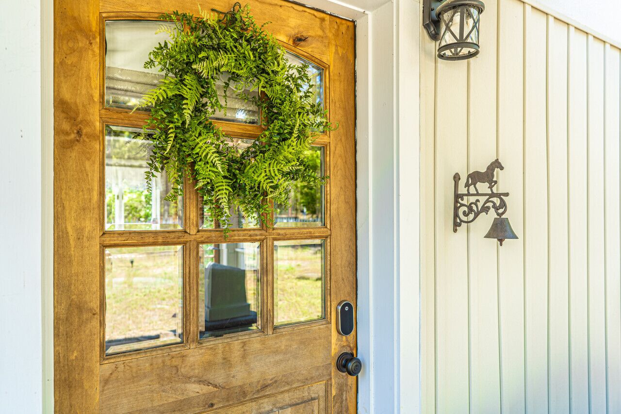 A wooden door with a glass panel and a wreath, a bell, and a lantern on the wall.