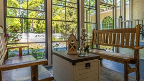 A wooden bench and a small table with a lantern and flowers in a sunlit room with large windows.
