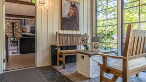 A wooden bench with a rustic design, a small table with a vase, and a large window with a view of greenery.