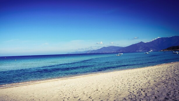 Una platja amb aigua blava cristal·lina, barques i muntanyes al fons.