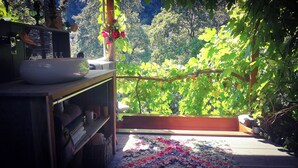 Habitació amb vista a un jardí exuberant, una taula de fusta amb una safata i una làmpada, i una catifes colorida al sòl.