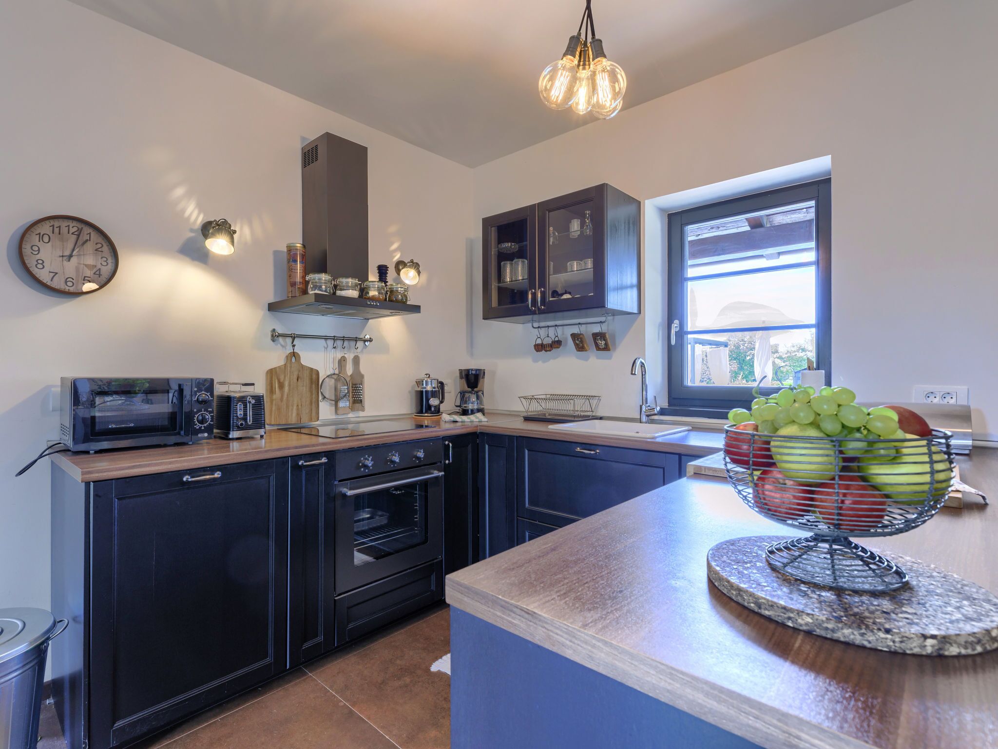 A modern kitchen with a central island, built-in oven, microwave, and a hanging light fixture.