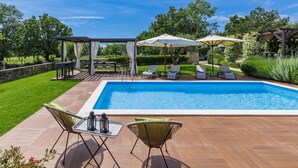 Ein Swimmingpool mit Liegestühlen und Sonnenschirmen, umgeben von einer Holzterrasse und einer Steinmauer.