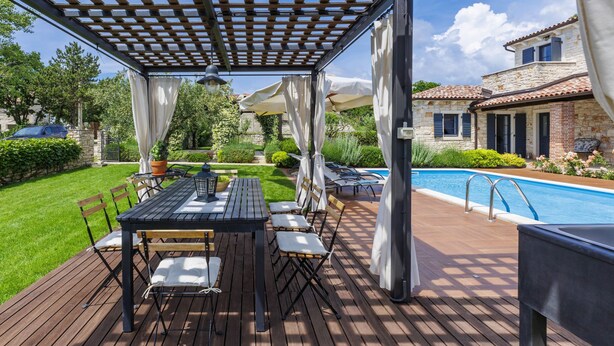 Eine Holzterrasse mit einer Pergola, Sitzgelegenheiten im Freien und einem Swimmingpool.
