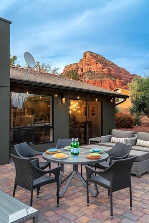 An outdoor patio with a round table and chairs, a built-in grill, and a view of red rock formations. - High-end 3BR Home w/ Spa, Firepit & Red Rock Views (Sedona)