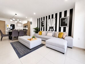 A modern living room with a sofa, ottoman, and dining area with chairs and a table.