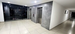 Un pasillo moderno con un vidrio que da a vistas de la ciudad, dos ascensores y piso de baldosas.