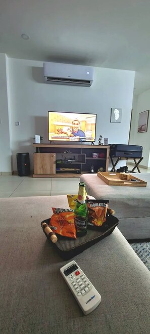 Una sala de estar con televisión, control remoto, bocadillos y un altavoz sobre un mueble de madera.