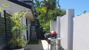 A dog walking on a concrete path in a backyard with potted plants, a barbecue grill, and a white wall. - Broadbeach Tropical Gem with Lux features (Broadbeach Waters)