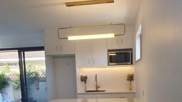 A modern kitchen with white cabinets, a stainless steel microwave, and a central island with a sink. - Broadbeach Tropical Gem with Lux features (Broadbeach Waters)