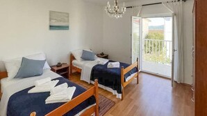 Ein Schlafzimmer mit zwei Betten, einer Kristallleuchtre, einem Balkon mit Aussicht und einem Gemälde an der Wand.