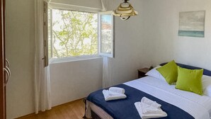Ein Schlafzimmer mit Bett, Kissen, einem Nachttisch, einem Fenster und einer Pendelleuchte.
