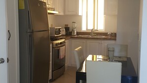 Una cocina con armarios blancos, un refrigerador de acero inoxidable, un horno, un fregadero y una mesa de comedor con sillas.
