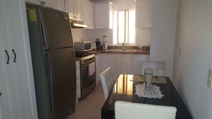 Una cocina compacta con armarios blancos, un refrigerador de acero inoxidable, una estufa y un lavamanos.