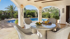 A covered outdoor area with a pool, wicker furniture, and a view of a hillside. - Navarra by Interhome (Moraira)