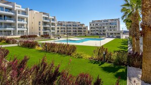 A modern hotel with multiple balconies, a central swimming pool, and well-maintained gardens.