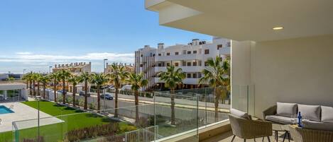 Un balcón con vista a una piscina, palmeras y edificios.