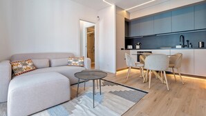 A modern living room with a sofa, a coffee table, and a dining area with chairs. - Ideal long stay: central, parking and pool (Sant Pol de Mar)