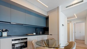 A modern kitchen with a glass dining table and chairs, a built-in oven, and a blue backsplash. - Ideal long stay: central, parking and pool (Sant Pol de Mar)