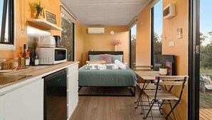 A compact room with a bed, a small kitchenette, and a dining area with a table and chairs.