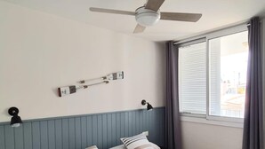 Une chambre d’hôtel avec un lit, un ventilateur de plafond, une fenêtre avec des rideaux et une lampe fixée au mur.