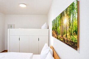 A bedroom with a bunk bed, a wardrobe, and a forest-themed wall art.