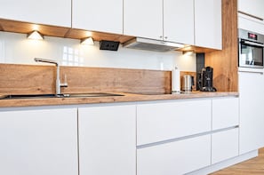 Eine moderne Küche mit weißen Schränken, einer Holz Arbeitsplatte, einem eingebauten Kochfeld und Beleuchtung unter den Schränken.