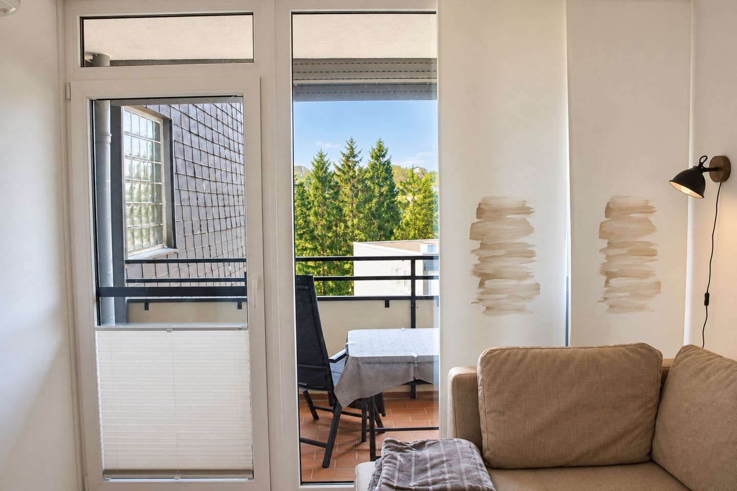 Une pièce dotée d’une porte-fenêtre coulissante donnant sur un balcon, d’un canapé, d’une table avec une chaise et d’œuvres d’art abstraites accrochées au mur.