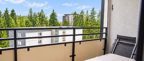 A balcony with a table and chairs, overlooking a residential area with trees and buildings.