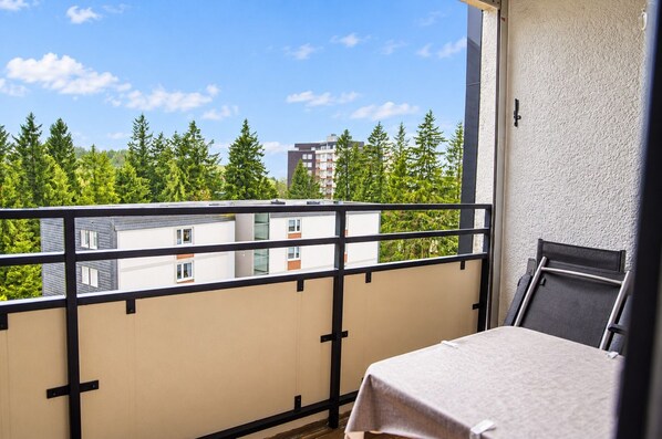Un balcón con mesa y sillas, con vista a una zona residencial con árboles y edificios.