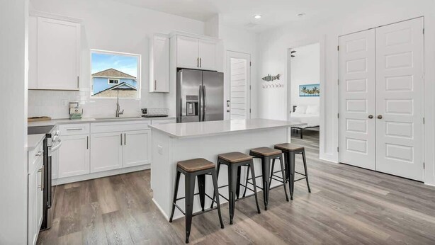 A modern kitchen with white cabinetry, a stainless steel refrigerator, and a bar area with stools. - Twente Toes (Navarre)