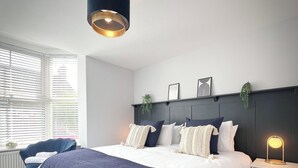 Une chambre moderne avec un grand lit, une table de chevet avec une lampe, une chaise et une fenêtre avec des stores.