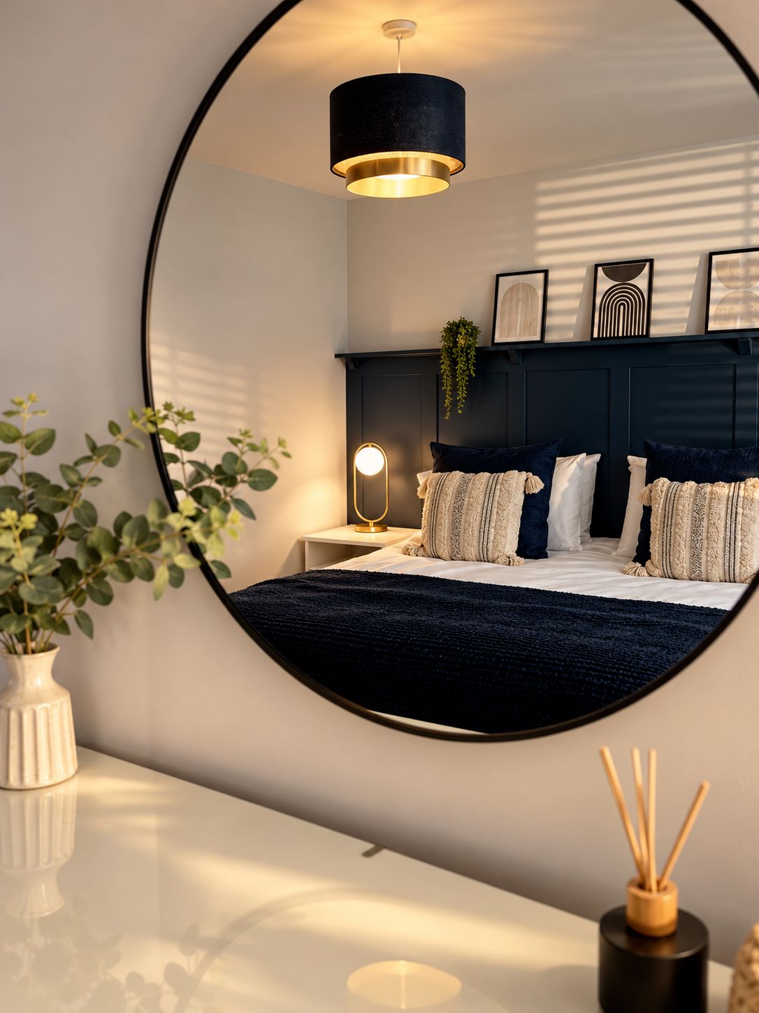 A bedroom with a bed, bedside table, lamp, and a mirror reflecting the room.