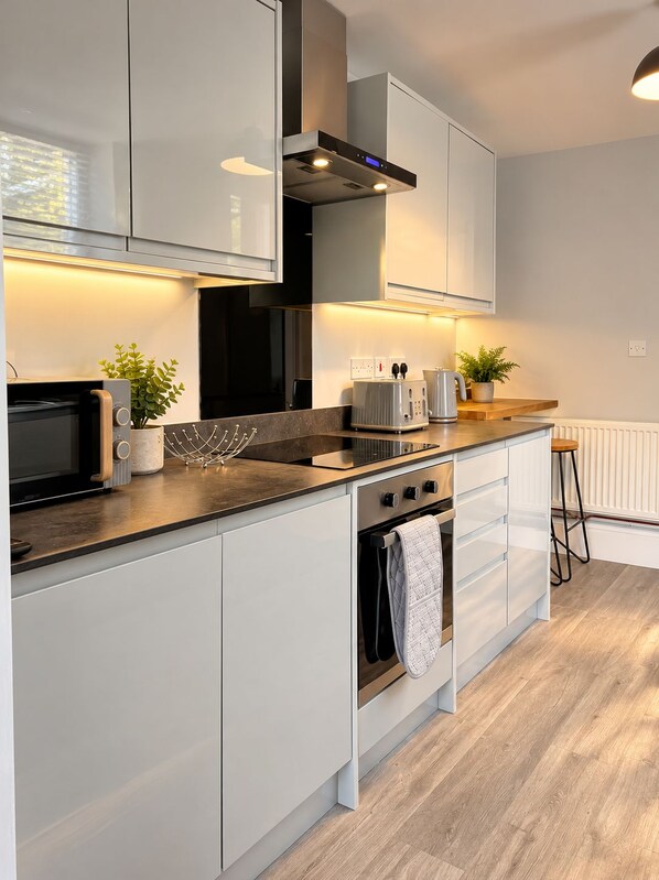 A modern kitchen with white cabinets, a built-in oven, a microwave, and a toaster. - Campbells Crib (Maidstone)