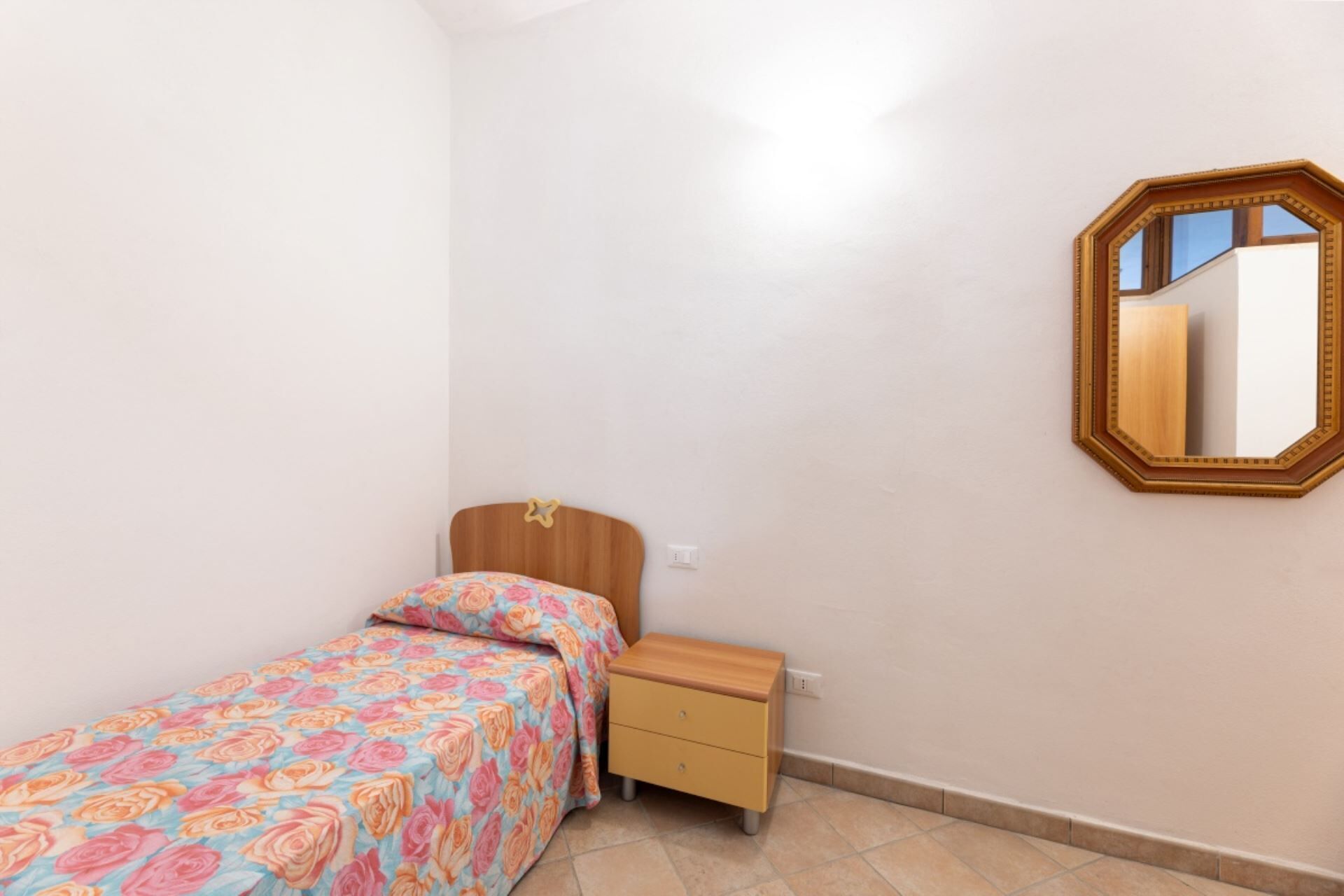 A small, neatly arranged bedroom with a single bed, a nightstand, and a mirror on the wall.